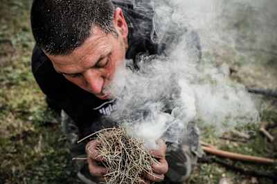 Homem sopra palha para potenciar o fogo.
