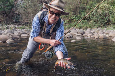 Person holds trout out the water in a stream in Australia.