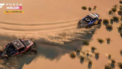 Screenshot aus Forza Horizon 5 Rally Adventure zeigt zwei Buggies in der Wüste, die beim Driften Sand aufwirbeln.