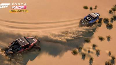 Screenshot aus Forza Horizon 5 Rally Adventure zeigt zwei Buggies in der Wüste, die beim Driften Sand aufwirbeln.
