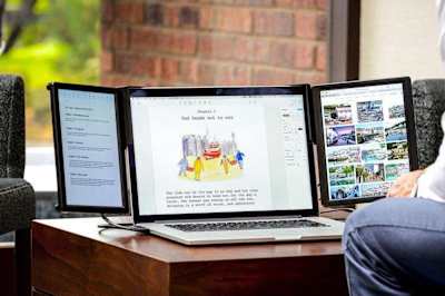 A man photographed facing a laptop with three different display screens