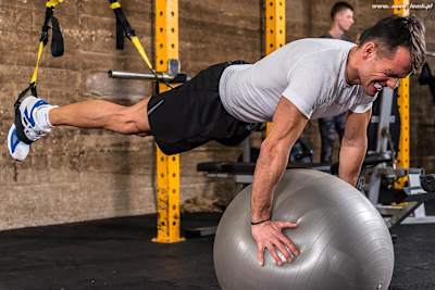 An athlete does a plank with an exercise bike using TRX straps.