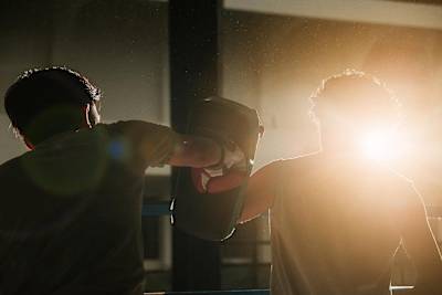 A photograph of two men hitting pads in a boxing ring