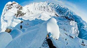 Travis Rice stands atop of snow-covered mountain.