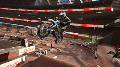 Screenshot aus MX vs ATV Legends zeigt zwei Motocross-Bikes, die im Stadion über eine Sprungschanze fliegen