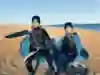 Two people lunge and pose with kitesurfing equipment.