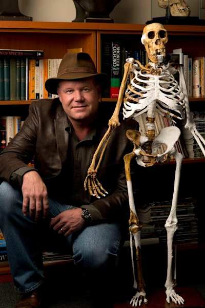 Lee Berger crouches down next to a sediba skeleton in a library.