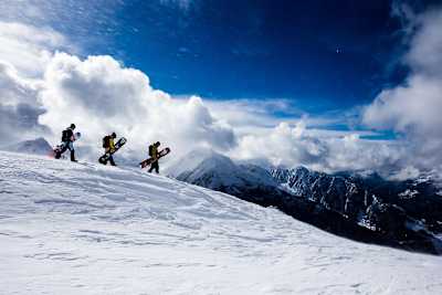 Travis Rice is joined by two other snowboarders at the top of a mountain.