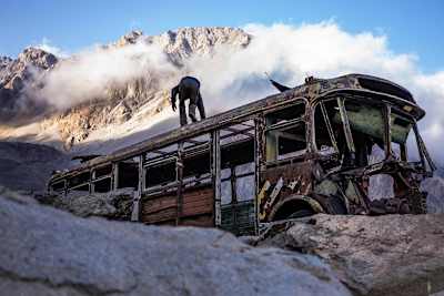 Man climbs on an old bus wreck high in the mountains.
