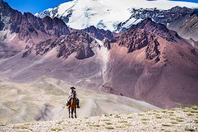 Man on horse seen in front of looming mountainous landscape.