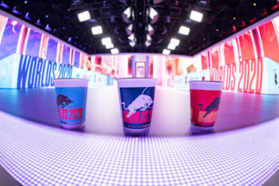 Trois verres Red Bull aux couleurs des Worlds 2020 de League of Legends sont disposés devant la scène de la compétition.