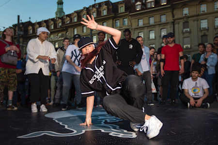 Jazzy Jes is doing footwork on a branded floor. People are standing in the background.