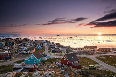 Sunset shot from Ilulissat, Greenland with traditional houses and ice caps floating in the background.