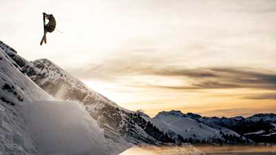 Manon Loschi s’envole en ski freestyle au-dessus des Alpes enneigées au coucher du soleil.