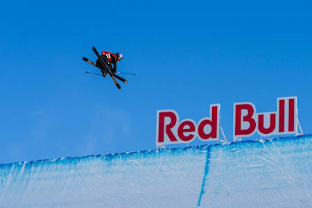 Eileen Gu s’élève dans les airs lors d’une session de ski freestyle, exécutant une figure spectaculaire sur un halfpipe Red Bull.