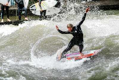 Eine Frau zeigt am Eisbach in München ihr Können beim Surfen der stehenden Welle.