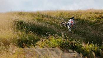 Brandon Semenuk pulls a trick over a jump near meadows in Japan.