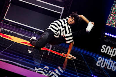 Shinshan is on the floor and holds one leg with a hand that reaches behind his head.