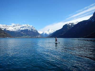 Ein Standup-Paddler paddelt vor schöner Bergkulisse auf einem See in der Schweiz.