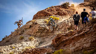 Cam Zink zjeżdżający z góry, w tle inny zawodnik wspinający się z rowerem, podczas Red Bull Rampage 2019 w Utah (USA).