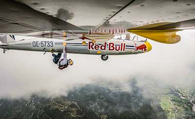 Domen Škofic hangs from a climbing hold beneath the wing of a Blanik glider.