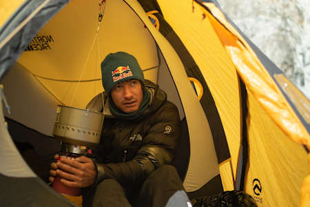 David Lama warms his hands on cooking equipment while sat in a tent.