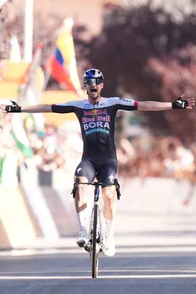 Nico Denz of Red Bull - Bora - Hansgrohe celebrates victory on stage 18 at the Giro d’Italia 2025, finishing in Cesano Maderno, Italy, with arms aloft and an ecstatic crowd in the background.