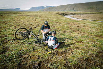 Двоє мотоциклістів ремонтують спущену шину  під час їзди.