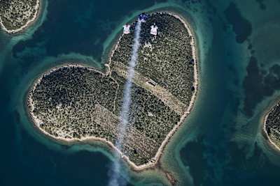 Marco Waltenspiel, Amy Chmelecki y Marco Fuerst vuelan con sus trajes de alas por encima de una isla con forma de corazón, cerca de Zadar, Croacia, el 30 de noviembre de 2016.