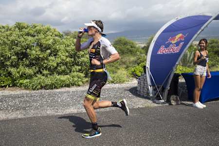 Triathlet Sebastian Kienle trinkt während des Ironman 2017 beim Laufen eine Red Bull Dose.