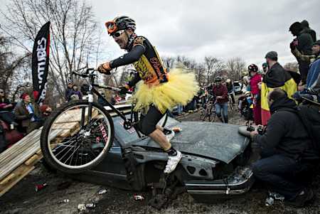 Un competidor de ciclocross supera un coche a modo de obstáculo en el Bilenky Junkyard Cyclocross 2013.