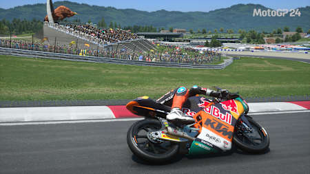 Screenshot aus MotoGP 24 zeigt ein Rennen der Moto3 am Red Bull Ring mit dem stählernen Bullen im Hintergrund.