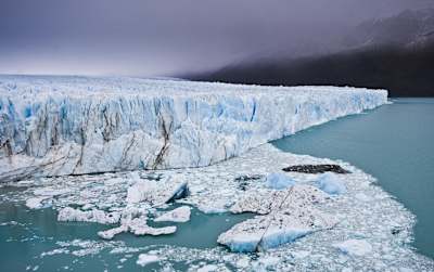 Massive glacier surrounded by clouds and fog rising into the water.