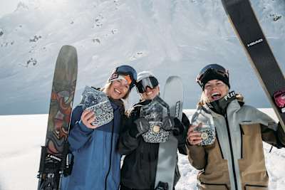 Winners Manon Loschi, Michelle Parker, and Hedvig Wessel celebrate with trophies at the Red Bull Natural Selection SKI competition in Alaska on March 26, 2025, against a dramatic mountain backdrop.