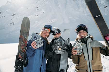 Winners Manon Loschi, Michelle Parker, and Hedvig Wessel celebrate with trophies at the Red Bull Natural Selection SKI competition in Alaska on March 26, 2025, against a dramatic mountain backdrop.