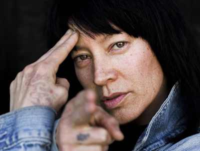 Asia One looking straight into the camera pointing at it with one hand while the other points to her forehead.