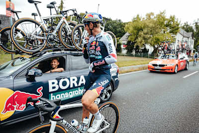 Un ciclista della Red Bull BORA - hansgrohe fa rifornimento accanto all'auto della squadra durante la seconda tappa del Deutschland Tour a Essen, in Germania, il 22 agosto 2025.