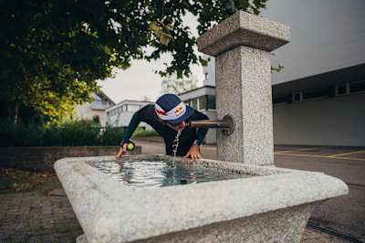 Ultrarunner Florian Neuschwander trinkt während einer Laufrunde Wasser aus einem Brunnen.