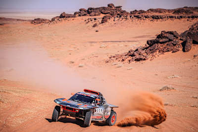 En 2024, Stéphane Peterhansel et Édouard Boulanger de l'équipe Audi Sport font courir leur Audi lors du Rallye Dakar en Arabie saoudite, en soulevant la poussière sur le terrain désertique.