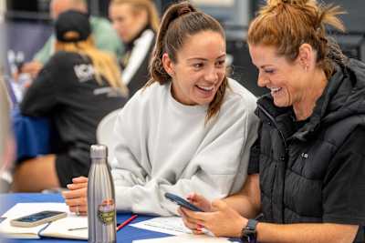 Two people chat at the Red Bull HYROX Coaches Camp in Silverstone, UK, on August 6, 2025. They engage in dynamic workshops, sharing training strategies and teamwork in preparation for competitions.