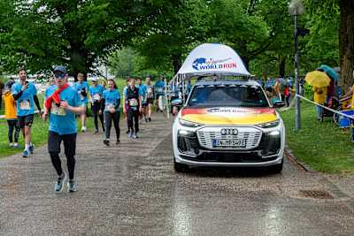 Participants in blue shirts take on the challenge at the 2025 Wings for Life World Run in Munich, Germany, as the official Catcher Car passes them in the rain.