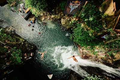 Aidan Heslop a Jonathan Paredes během Světové série Red Bull Cliff Diving 2026 skáčou ze stromu u vodopádu Kroya na Bali a předvádějí neohrožený sportovní výkon uprostřed nádherné tropické scenérie.