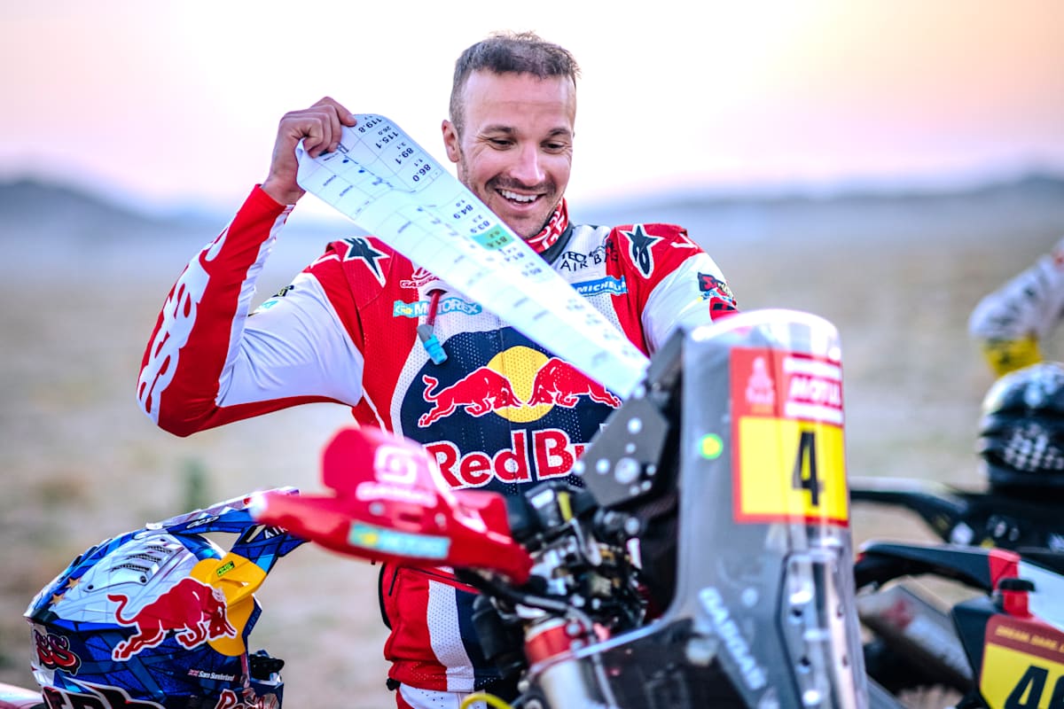 En 2024, Sam Sunderland, de Red Bull GAS GAS Factory Racing, radiante de alegría, sostiene su roadbook de rally en la línea de salida de la etapa del Rally Dakar en Arabia Saudí.