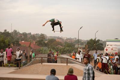 Madars Apse fliegt per Ollie über eine Jumpramp im Skatepark in Mukono, Uganda. Es sieht aus als wäre er hoch im Himmel, während die anwesenden Locals zu ihm hochblicken.