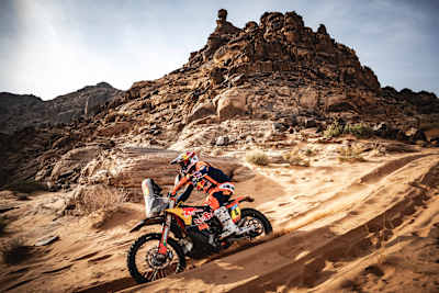 En la 2025, Daniel Sanders, de KTM Red Bull Factory Racing, corre con su moto por terreno arenoso con imponentes formaciones rocosas como telón de fondo durante la Etapa 5 del Rally Dakar.