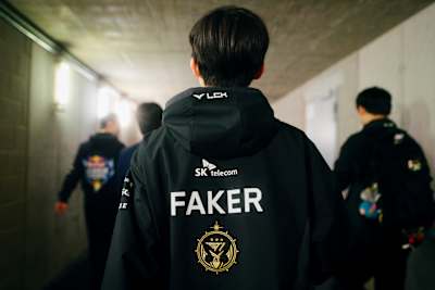 Faker, joueur emblématique de T1 sur League of Legends, traverse un couloir vêtu de la veste de son équipe.