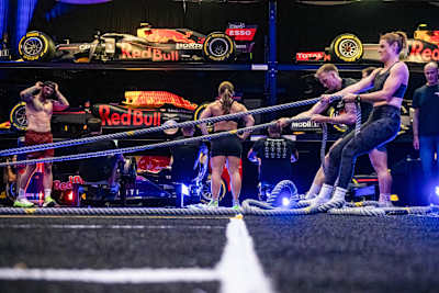 Athletes test their endurance in the sled pull at the Red Bull HYROX coaches camp 2025, surrounded by Red Bull Racing Formula One cars at Silverstone Circuit, UK.