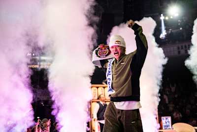 A victorious moment as the Red Bull BC One champion, Issin, raises his arms and trophy in Tokyo, surrounded by smoke effects, at the thrilling 2025 season finale.