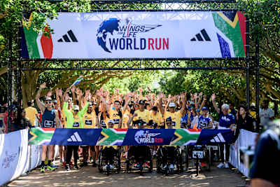 Participants at the 2024 Wings for Life World Run App Run in Cape Town, South Africa, cheer enthusiastically under a vibrant arch, ready to start the iconic global event