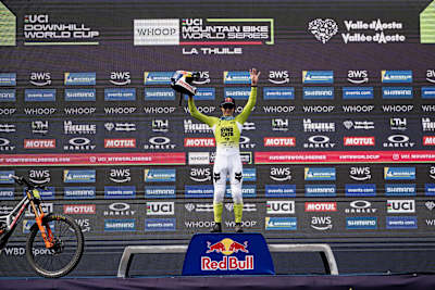 Jackson Goldstone celebrates his victory at the UCI Mountain Bike World Cup 2025 in La Thuile, Italy, raising his helmet on the podium.